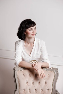 Beyaz tişörtlü ve kırmızı pantolonlu çekici genç bir kadının stüdyo portresi düz beyaz arka planda klasik bir sandalyeye dayanıyor. Patronluk taslayan kadın, iş görüşmesi konsepti, kendine güvenen bağımsız kadın..