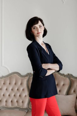 Kollarını kavuşturmuş güzel, esmer bir kadın. Kısa saçlı, siyah ceketli ve kırmızı pantolonlu bir kız..