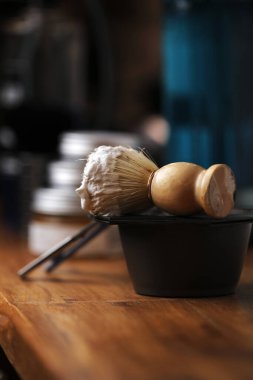 Tıraş ekipmanları ve erkeklerin kozmetik ürünleri ahşap masada, berber dükkanında. Traş makinesi, tıraş fırçası ve köpükle traş konsepti. Erkekler için sakal bakım ürünleri