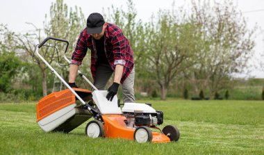 Günlük kıyafetli bir adam, kendi arka bahçesinde çim biçtikten sonra çim biçme makinesi kesilmiş bir çanta alır. Kocası bahçeyle ilgilenir. Modern benzin bahçesi ekipmanları. Evde peyzaj işi.