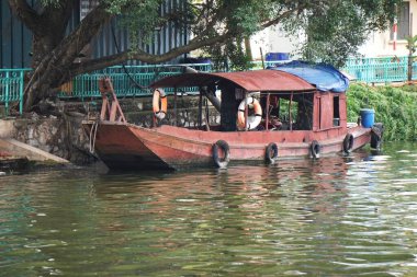 Hanoi Vietnam yakınlarındaki bir göl boyunca demirlemiş paslı bir çalışma teknesi. Yan taraflardan eski lastikler sarkıyor. Tamponlar ve mavi plastik muşamba kabini kaplıyor..