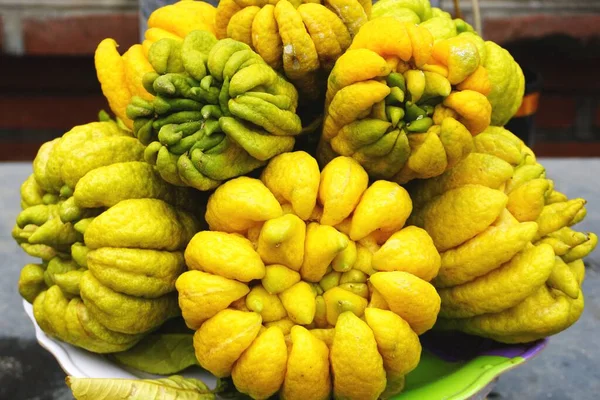 Olgun sarı tropik Buda Eli meyvesi Hanoi Vietnam yakınlarındaki bir Budist tapınağında bir tabağa istiflenmiş. Alışılmadık şekilli narenciye meyvesi yerel tapınaklarda yaygın bir duadır. Görünüşü, parmakları olan topak topak bir limon gibi..