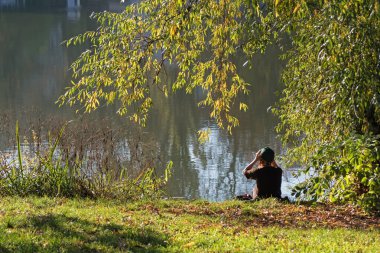 Berlin, Almanya - 7 Kasım 2020: Lietzen Gölü kıyısındaki Kuno-Fischer-Platz bahçeleri genç bir bayanla birlikte kıyıdaki sıcak sonbahar gününün tadını çıkarıyordu.
