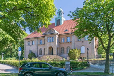 Berlin, Almanya - 3 Haziran 2021: Mimari anıt eski belediye binası Nikolassee itfaiye istasyonu ve park halindeki elektrikli araba şarj edilen şarj istasyonu