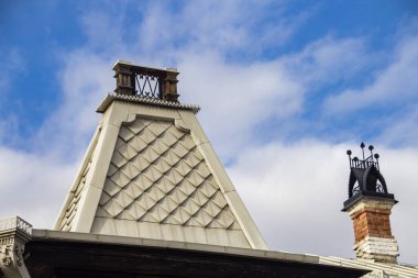 Eski taş bir malikanenin çatısında açık bulutlu mavi bir gökyüzüne karşı.