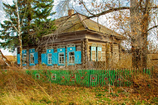 Lonely old log village house with green fence, autumn landscape, old architecture.
