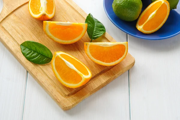 Segmentos de laranja com folhas na superfície de madeira branca — Fotografia de Stock