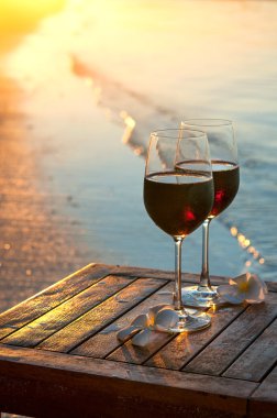Romantik sahil sahne: iki bardak kırmızı şarap suya yakın gün batımında