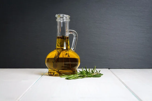 Botella de aceite de oliva, rama de romero fresco sobre mesa de madera blanca — Foto de Stock