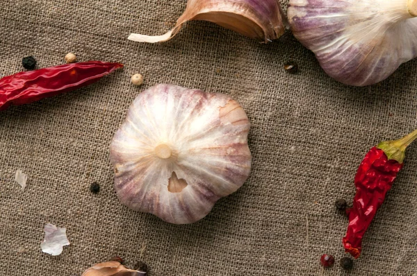 Garlic heads and red chili peppers on hessian fabric cloth background — Stock Photo, Image