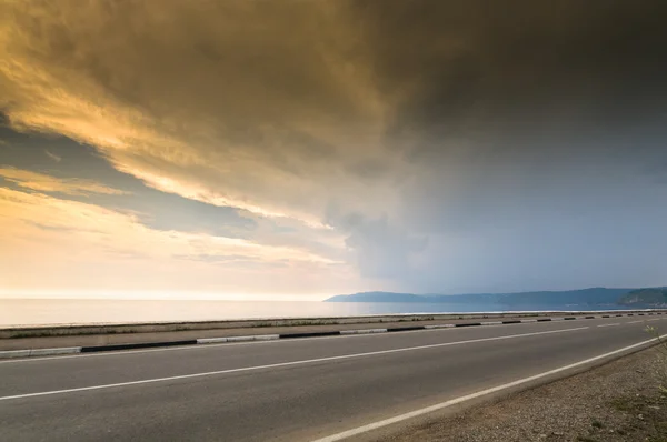 Long road and sea, lake or ocean line in sunset time with cloudy sky