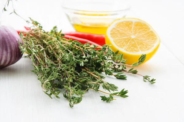 Gelbe Zitronenhälfte, grüner Thyn-Zweig Chilischote, Olivenöl, Knoblauchkopf auf weißem Holztisch oder isoliert — Stockfoto