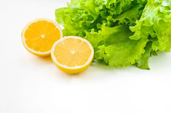 Yellow lemon half and green leaf lettuce on white wooden table or isolated — Stock Photo, Image