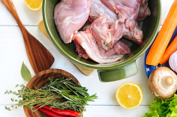 Översta platt vy av rå kaninkött med grönsaker i runda keramiska potten på vitt trä bord yta — Stockfoto