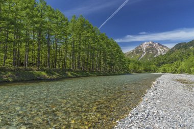 Azusa Nehri 'nin el değmemiş alp suları, Japonya' nın Kamikochi, Nagano şehrinde güneşli, mavi bir gökyüzü gününde Hotaka-Dake Dağı 'nın manzarası önünde akıyor..