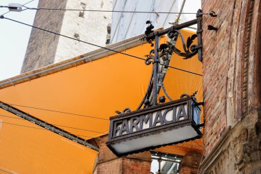 Eczane, Bologna, İtalya 'da Farmacia imzası. Tuğla bir binanın üzerinde dövülmüş demir bir tabela.