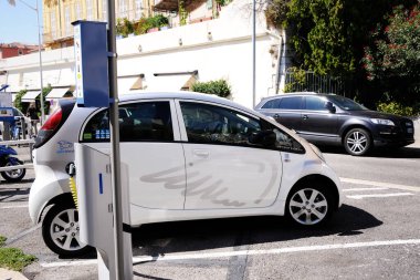 A white mini-electric car is charged on street charging.