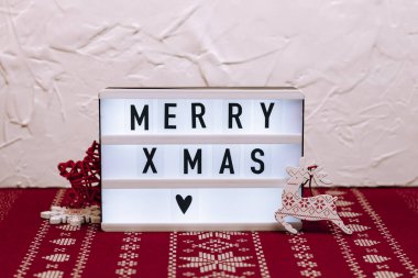 Beyaz beton ve kırmızı yılbaşı desenli arka planda küçük ışık kutusu. Tahta Noel oyuncakları.