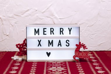 Beyaz beton ve kırmızı yılbaşı desenli arka planda küçük ışık kutusu. Tahta Noel oyuncakları.