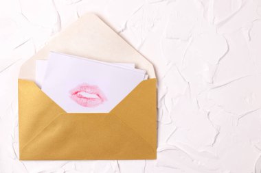 Beyaz desenli arka planda, altın bir zarfta pembe ruj izi olan bir aşk mektubu. Öpüşme Günü, Sevgililer Günü, sevdiklerine bir hediye. Kartpostal, pankart, kopyalama alanı.
