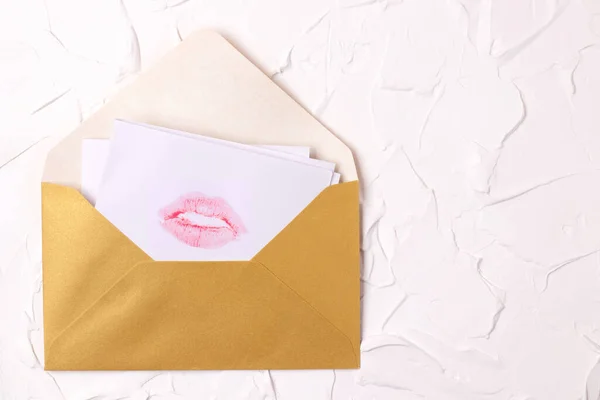 Love letter with a print of lips made by pink lipstick in a gold envelope on a white textured background. Kissing Day, Valentine\'s Day, a gift to a loved one. Postcard, banner, copy space.