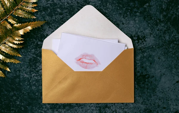 Love letter with a print of lips made by pink lipstick with golden leaves on the textured background . Kissing Day, Valentine's Day, a gift to a loved one. Postcard, banner, copy space.