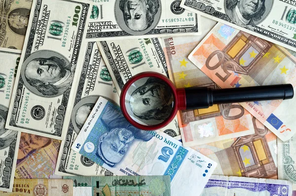 Strewn banknotes with a magnifier — Stock Photo, Image