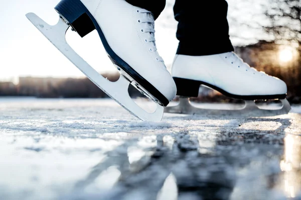 Woman wearing white figure skates stands on ice. Winter outdoor sport activities