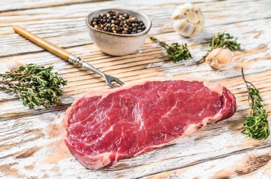 New York bifteği ya da otlu striploin, çiğ sığır eti. Beyaz ahşap arka plan. Üst görünüm.
