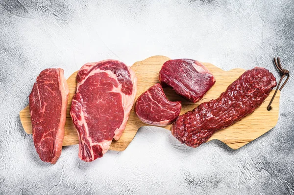 Variety of raw black angus beef meat steaks fillet Mignon, rib eye or cowboy, Striploin or new york, skirt or machete. White background. Top view.