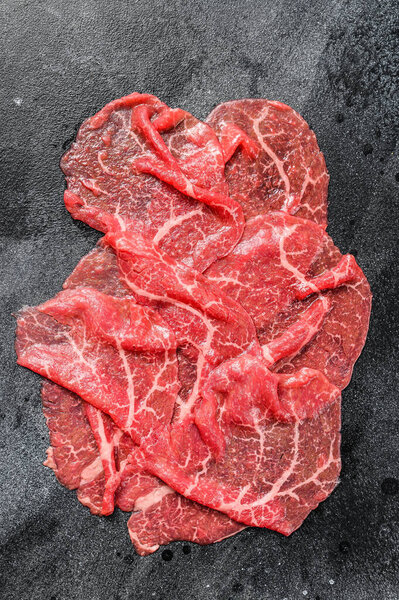 Кусочки говядины Каприччио, сырое мясо. Чёрный фон. Вид сверху.