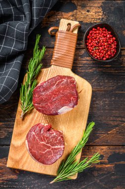 Kesme tahtasının üzerinde çiğ biftek fileto fileto. Karanlık ahşap arka plan. Üst görünüm.
