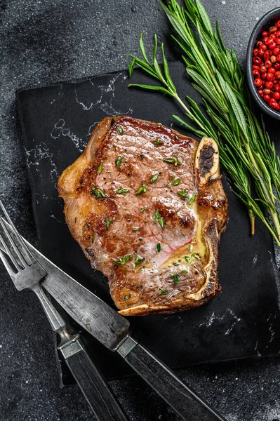 Grilled striploin steak on the bone or new york steak. Black background. Top view.