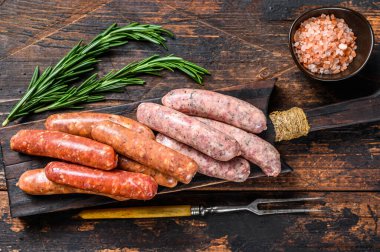 Kesme tahtasındaki çiğ sosisler. Koyu ahşap arka plan. Üst görünüm.