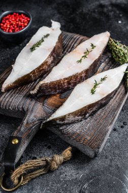 Tahta bir tahtanın üzerinde çiğ taze halibut balığı bifteği. Siyah arka plan. Üst görünüm.