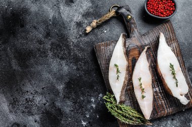 Tahta bir tahtanın üzerinde çiğ taze halibut balığı bifteği. Siyah arka plan. Üst Manzara. Boşluğu kopyala.