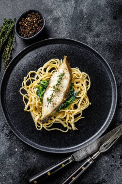 Fırınlanmış Halibut balığı bifteği ve ıspanaklı makarna. Siyah arka plan. Üst görünüm.