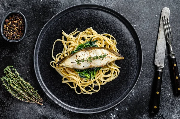 Spaghetti pasta with Halibut fish steak and spinach. Black background. Top view.