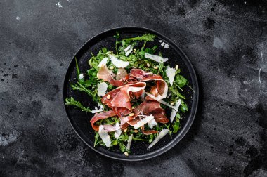 Parmalı salata, jambon, roka ve parmesan peyniri. Siyah arkaplan, üst görünüm, metin için boşluk.