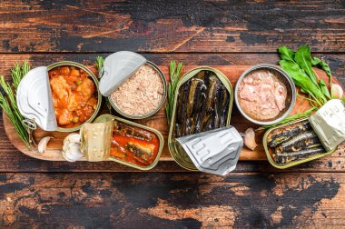 Açılmış kutular saury, somon, sprat, sardalya, kalamar ve ton balığıyla korunur. Karanlık ahşap arka plan. Üst görünüm.