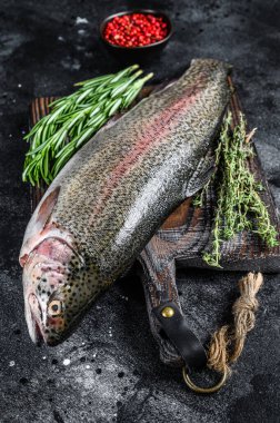 Kesme tahtasındaki çiğ Gökkuşağı alabalığı ve bitkiler. Siyah arka plan. Üst görünüm.