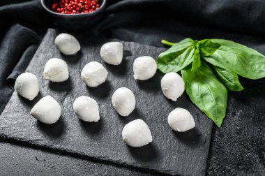 Üzerinde fesleğen yaprağı ve pembe biber olan taş bir tahtada mini mozzarella peyniri topları. Siyah arka plan. Üst görünüm.