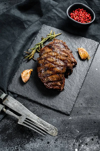 Grilled Flat Iron steak on a stone Board, marbled beef. Black background. Top view.
