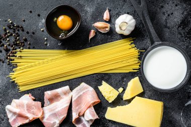 Geleneksel İtalyan alla carbonara makarna malzemeleri. Pişmemiş spagetti, pancetta pastırması, parmesan peyniri, yumurta. Siyah arka plan. Üst görünüm.