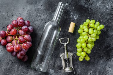 Bir dal yeşil ve kırmızı üzüm, bir şişe, bir tirbuşon ve bir mantar. Şarap yapma kavramı. Siyah arka plan. Üst görünüm.