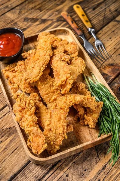 Breaded chicken breast tenders strips with ketchup. Wooden background. Top view.