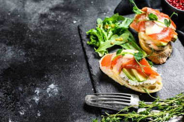 Avokado ve somonlu sağlıklı sandviç. Ispanak ve roka salatası. Siyah arka plan. Üst Manzara. Boşluğu kopyala.