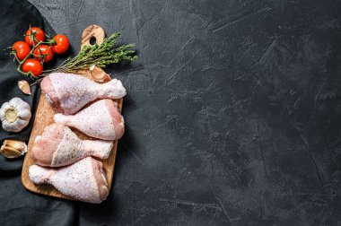 Tahta kesme tahtasına baharat ve sebze konmuş çiğ tavuk budu. Siyah arka plan. Üst Manzara. Boşluğu kopyala.