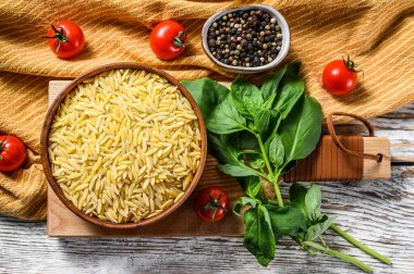 Bir kase çiğ Orzo makarna, fesleğen yaprağı, domates ve sarımsaklı. Beyaz arka plan. Üst görünüm.