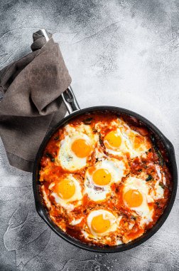 Ev yapımı shakshuka, kızarmış yumurta, soğan, dolmalık biber, domates ve tavada maydanoz. Gri arka plan. Üst görünüm.